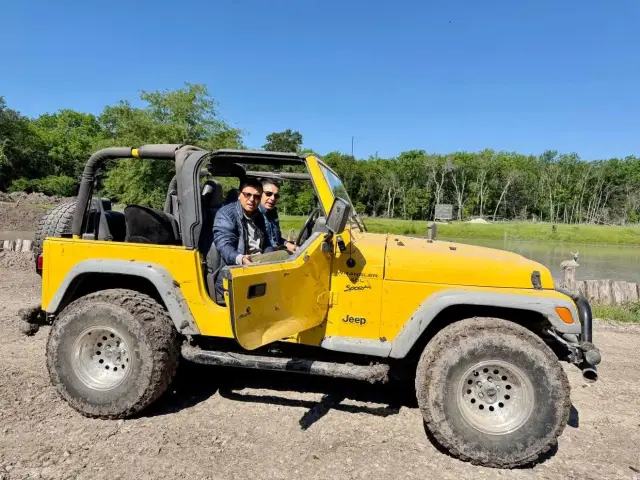 Two riders in a yellow Jeep Wrangler parked beside the pond.