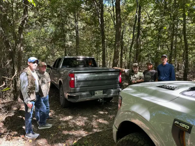 Friends standing by their pickup trucks on a shaded dirt trail.