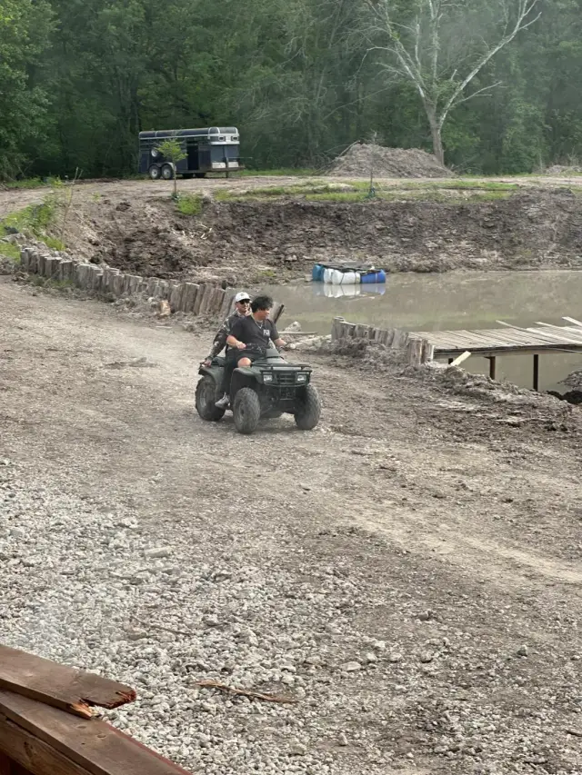 Two riders on an ATV cruising the gravel loop past the pond.