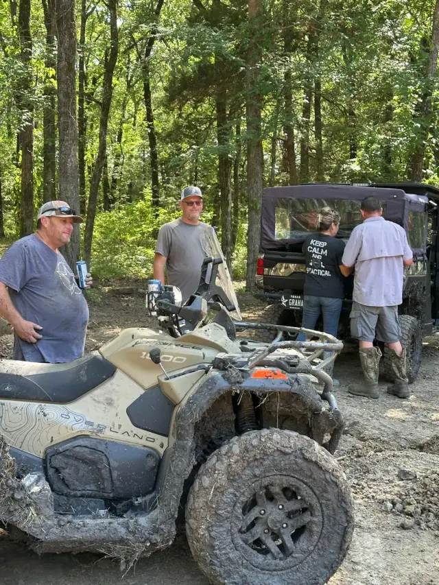 Riders gathered around a muddy CFMOTO ATV and side-by-side.