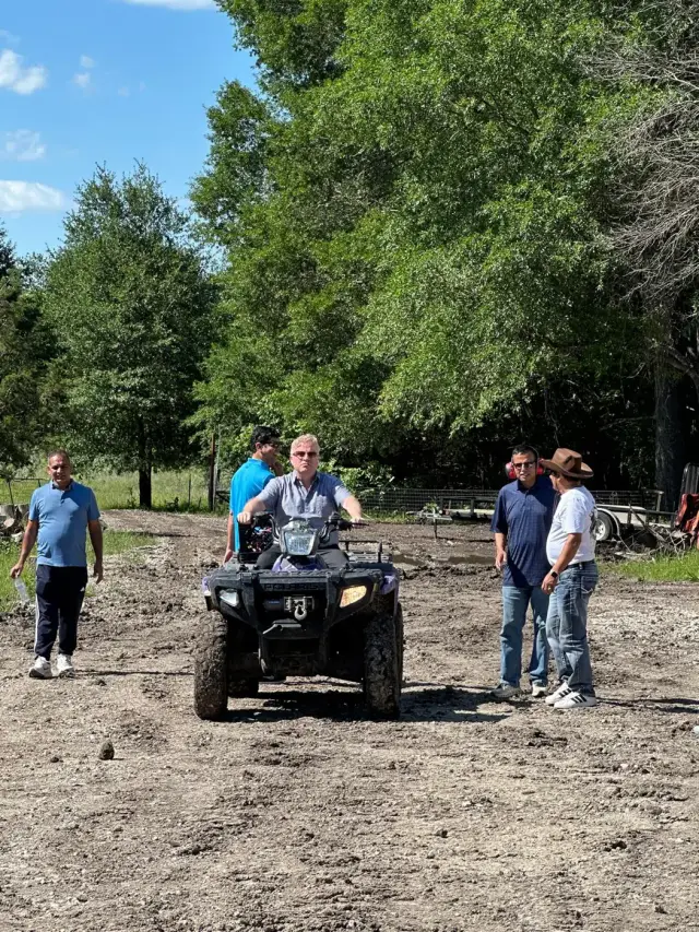 A rider on a Polaris ATV while friends watch from the yard.