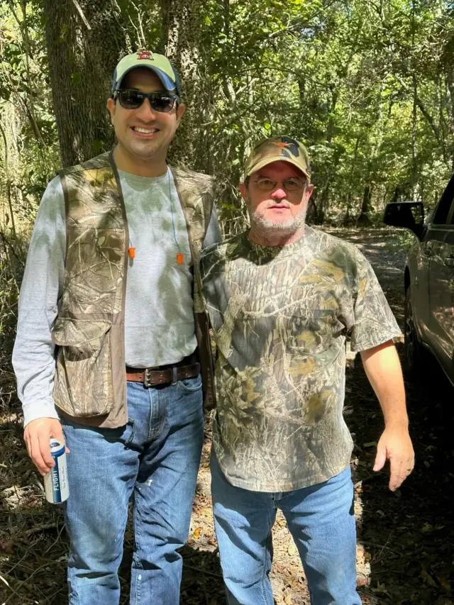 Two friends in camo standing on a shaded trail.