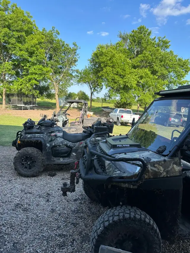 A camo CFMOTO ATV and a Polaris side-by-side parked on the gravel lot.